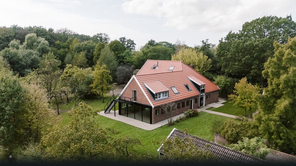 Hof van Kairos: een oude woonboerderij met rode pannendaken tussen de bomen, met tuin