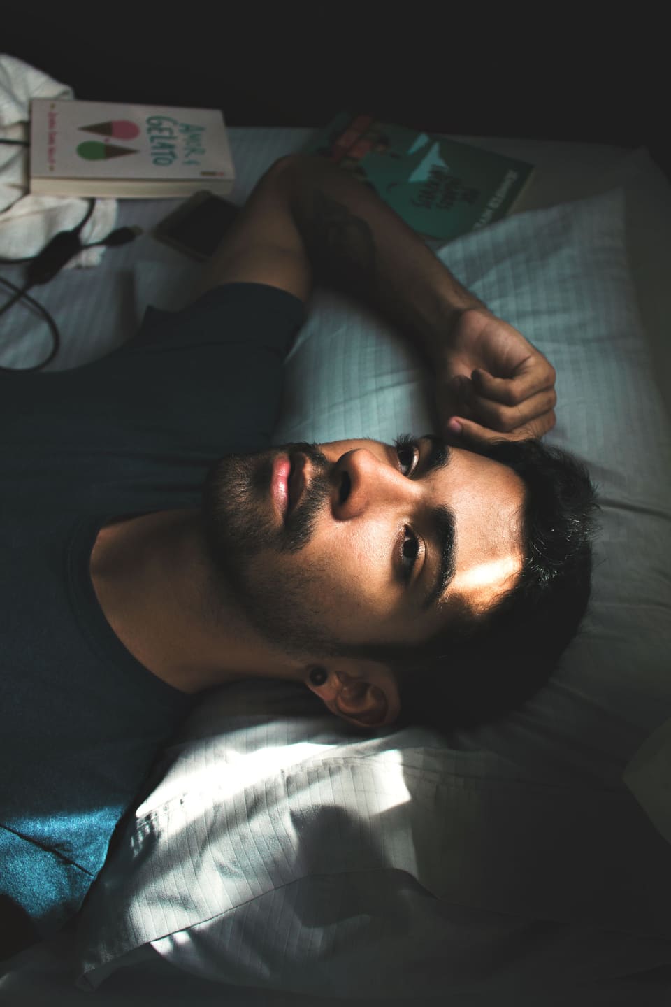Een man die wakker in bed ligt en naar boven kijkt, met boeken en zijn telefoon naast zijn kussen