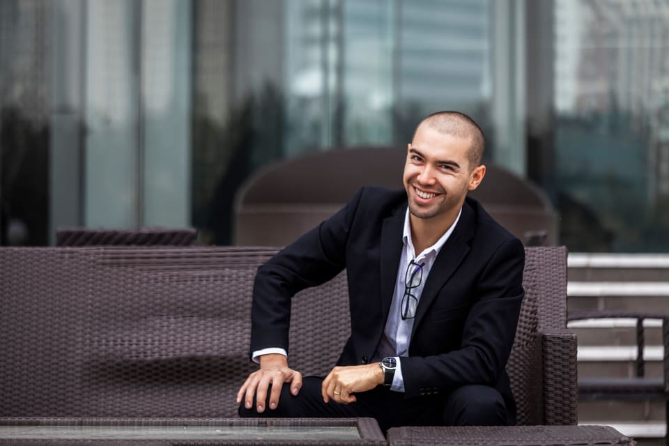Een lachende man in pak op een bank op een terras