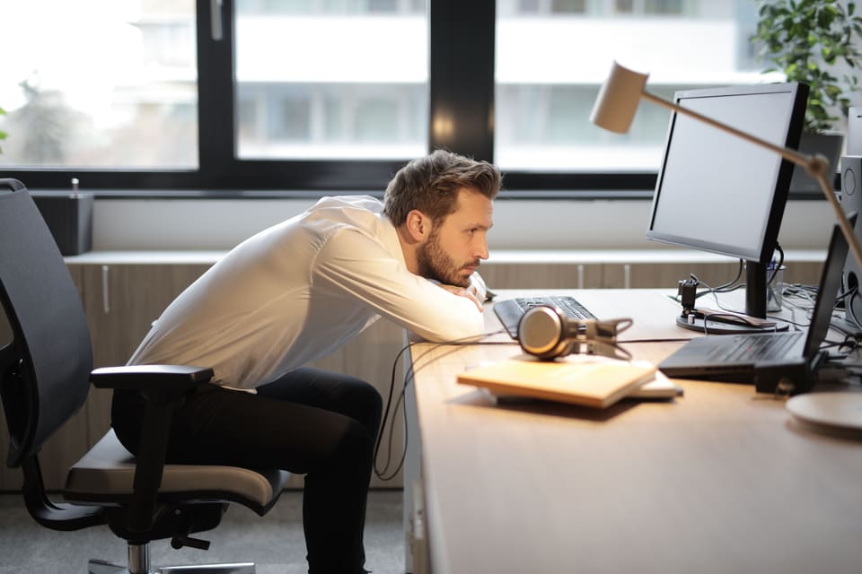 Een man in een wit overhemd die voorover over zijn bureau hangt en naar zijn beeldscherm staart